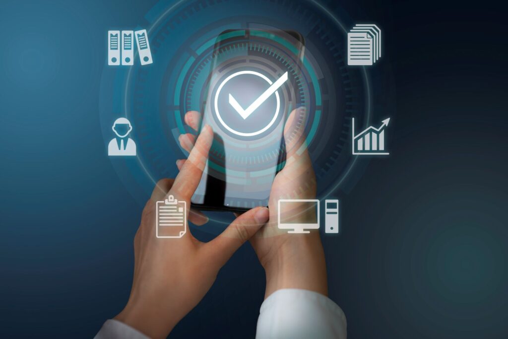Mãos segurando um smartphone com ícone de verificação e símbolos digitais ao redor, representando gestão de acesso.