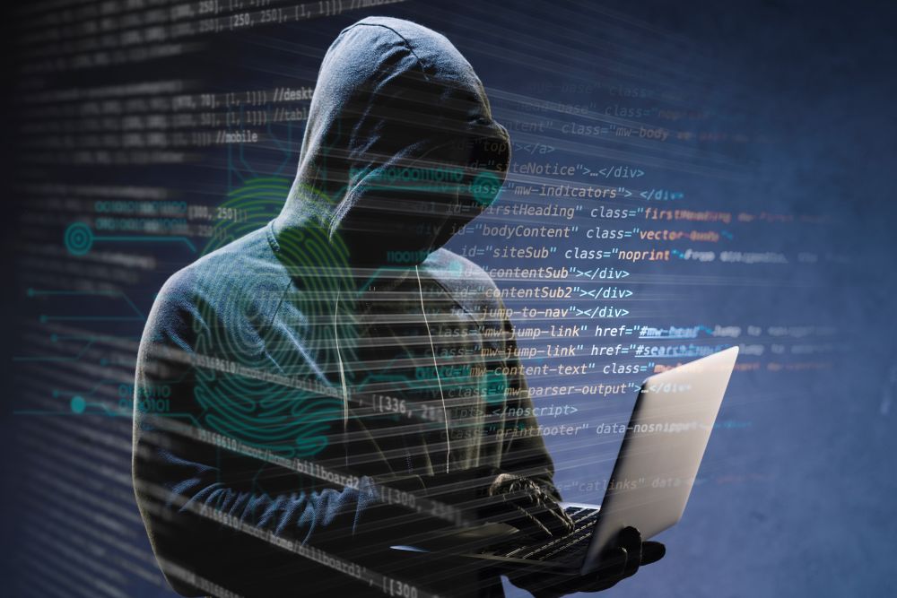Pessoa com capuz utilizando notebook em ambiente digital escuro, representando um ciberataque e ameaças virtuais contra sistemas empresariais.