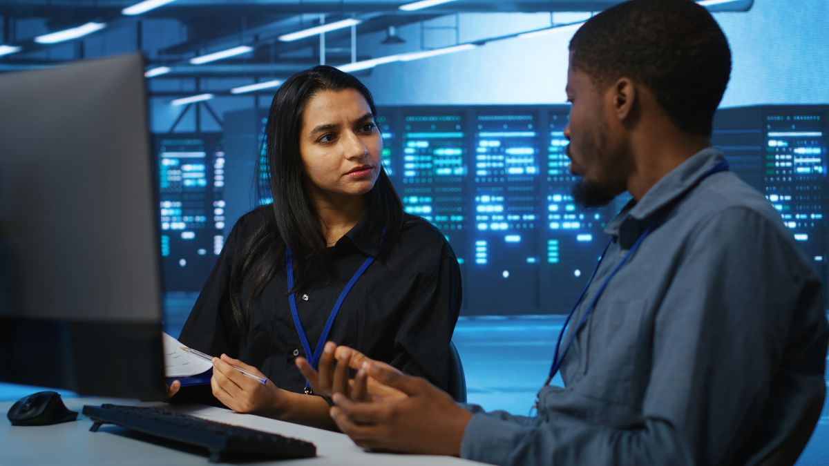 Dois profissionais de TI conversam em ambiente de data center durante consultoria em cibersegurança.
