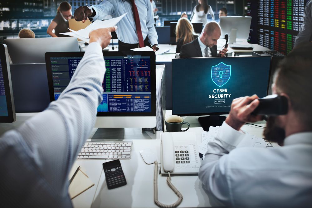 Equipe corporativa acompanha painel de cyber security em ambiente de operações tecnológicas.