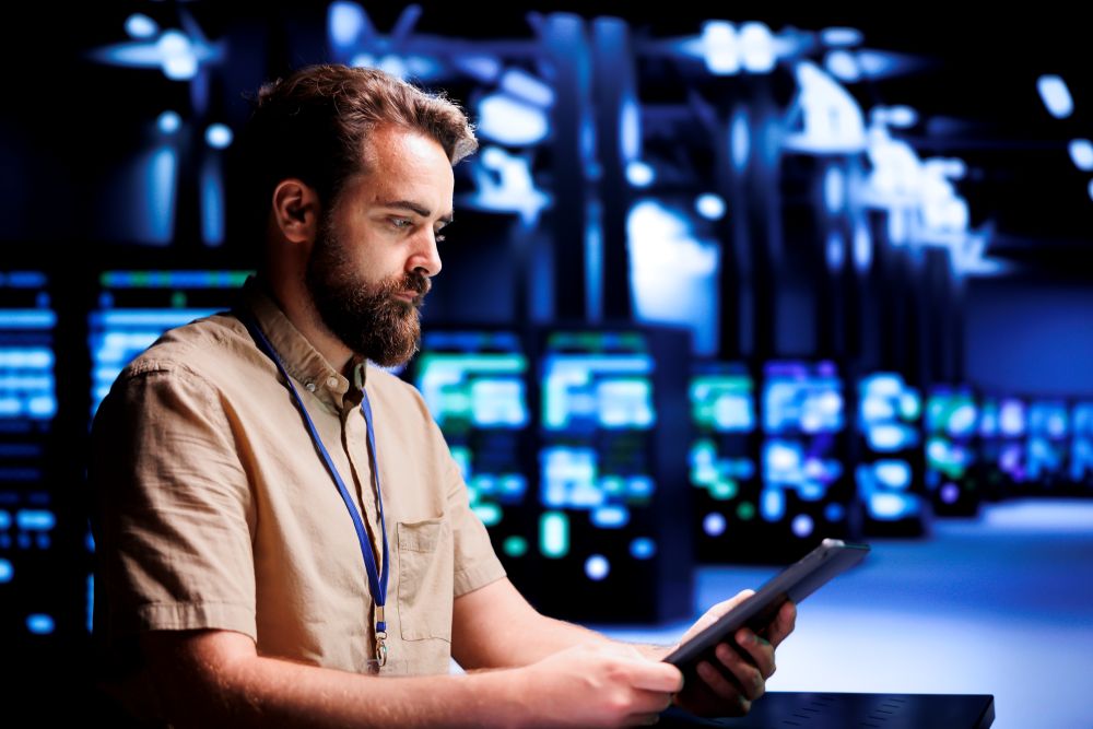 Profissional de TI analisa tablet em data center com servidores ao fundo.